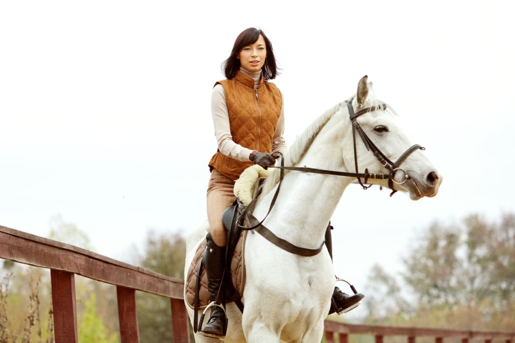 防寒着を着て白い馬に乗る女性